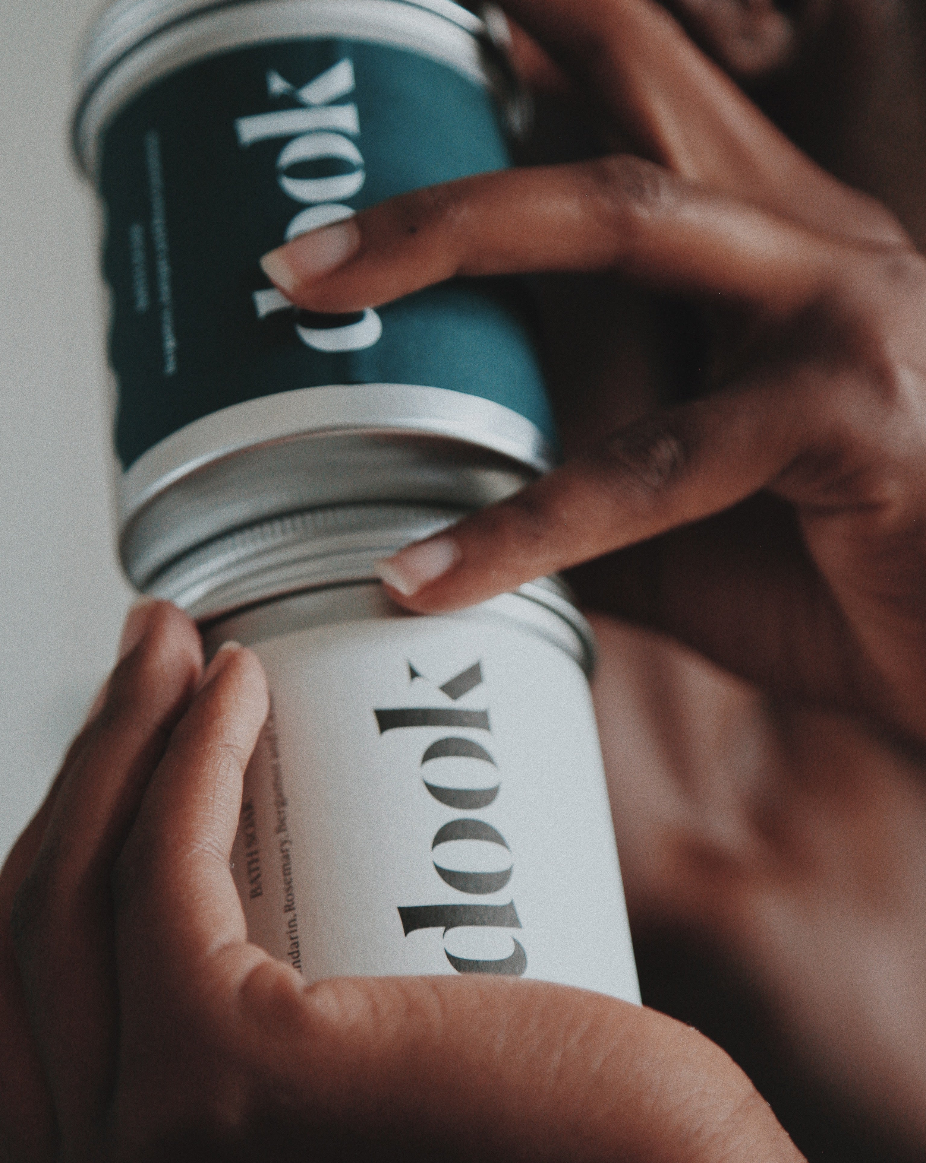 Two hands holding together two different tins of dook bath salts.