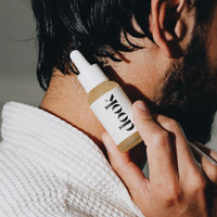 Profile of black haired man with beard holding a bottle of conditioning oil and presenting it on his neck.