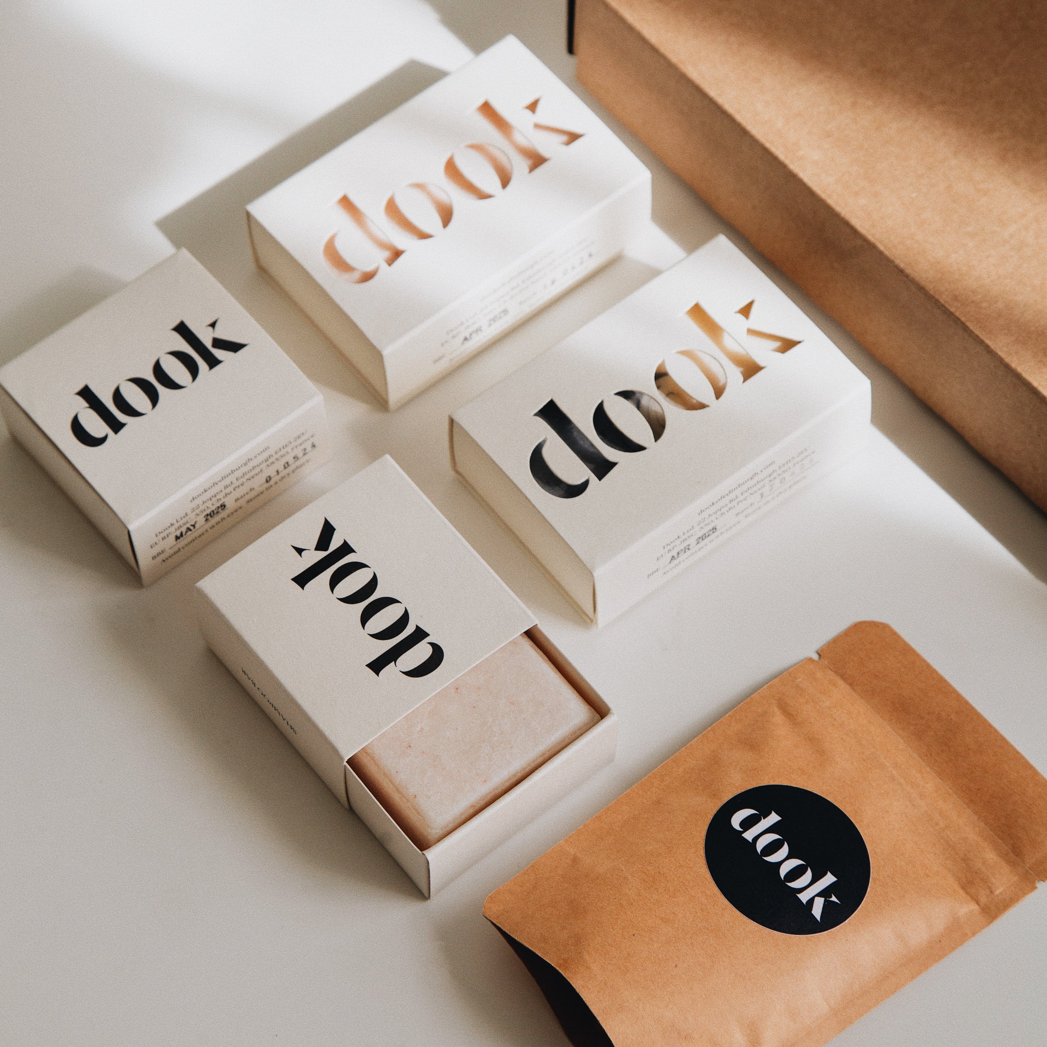 Subscription box offer of two soaps and two shampoo layered flat next to a brown box and a sample, product tester small paper bag.