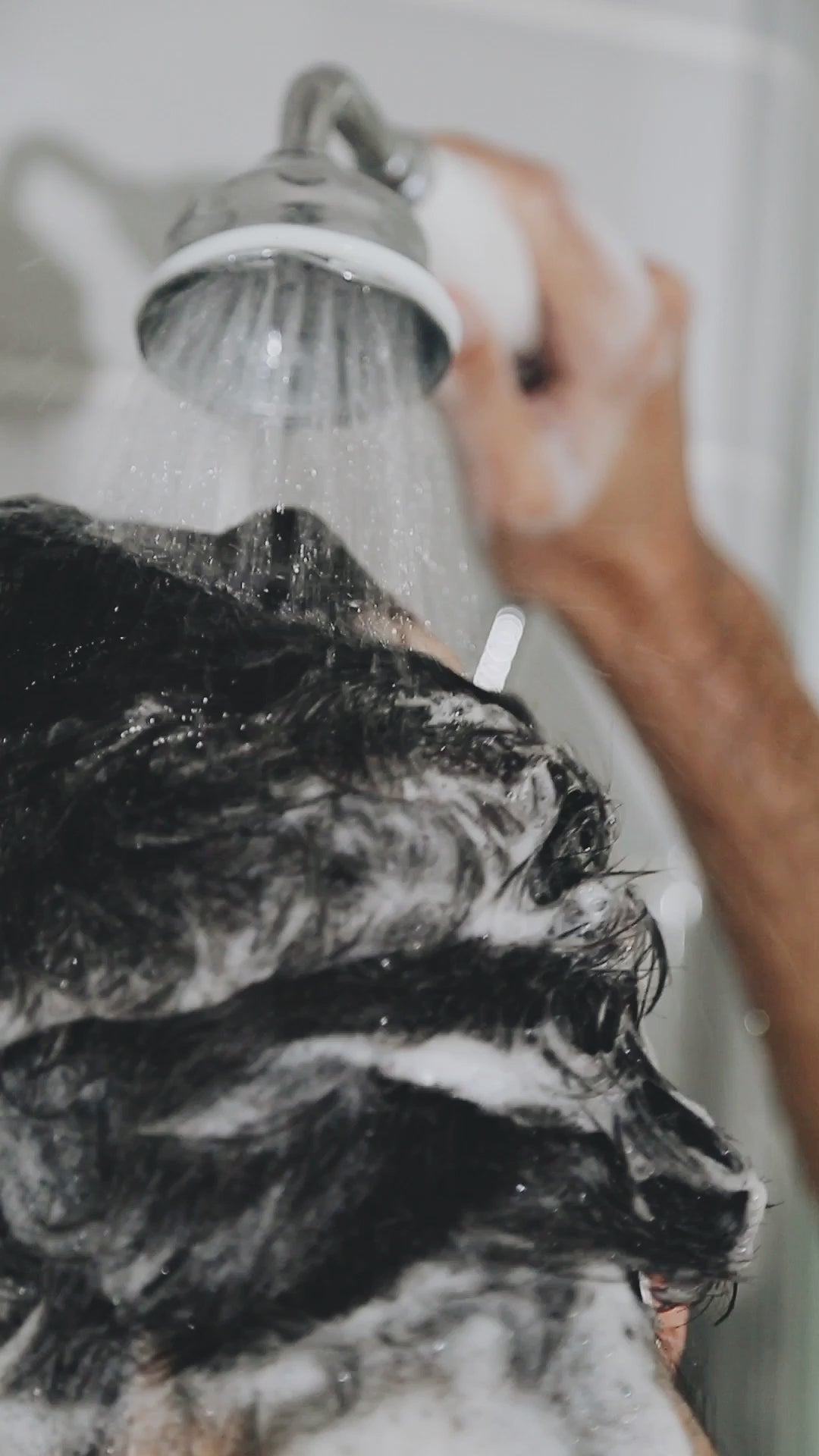 A man rinsing his black short hair under the shower.