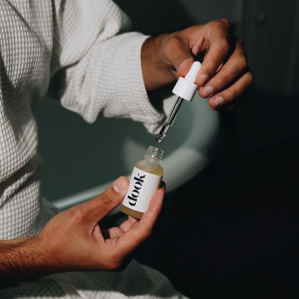 A person holding opened conditioning oil bottle. One hand holds the bottle and the other hand is exposing the pipette.