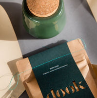 Green, handmade bath salts jar with cork lid and dook's bath salts in bag placed on grey surface.