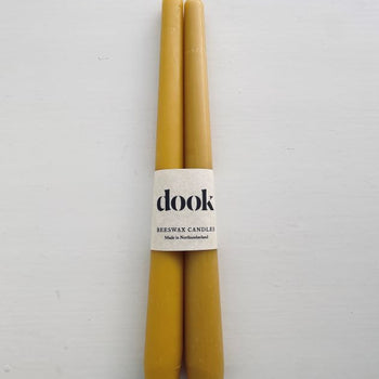 A pair of yellow, beeswax dining candles wrapped with natural creamy paper with black dook logo.