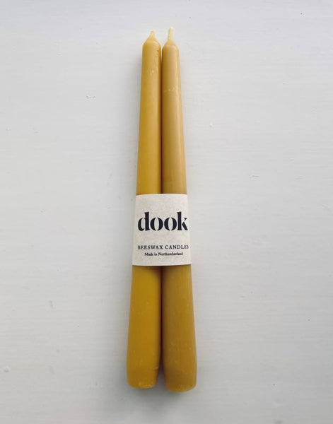 A pair of yellow, beeswax dining candles wrapped with natural creamy paper with black dook logo.