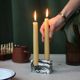 A hand placing lit beeswax dining candle in a double stone candle holder.