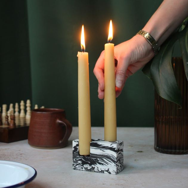 A hand placing lit beeswax dining candle in a double stone candle holder.