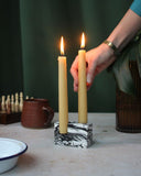 A hand placing lit beeswax dining candle in a double stone candle holder.