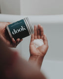 A person holding a tin with bath salts and emptying it on the hand palm. White bath tub and blurred bathroom background.