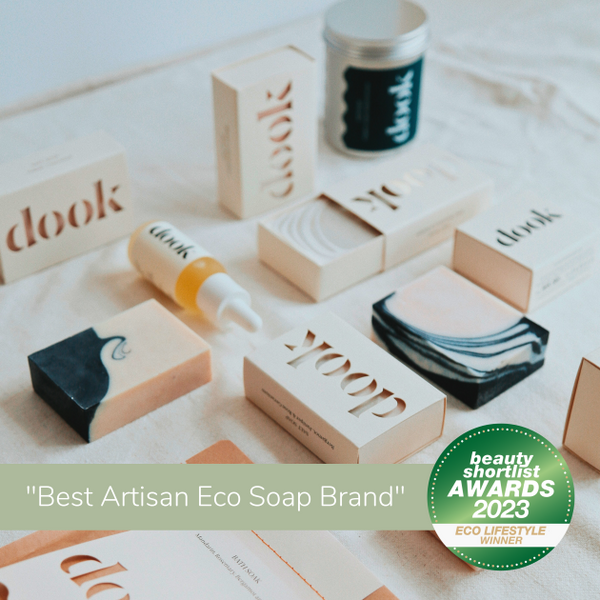 Range of dook products laying flat on white cloth. Picture marked with green stripe with title "Best Artisan Eco Soap Brand" beauty shortlist awards 2023.