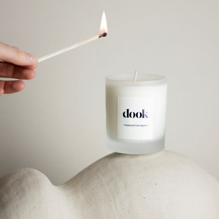 Hand holding a burning match above the dook candle. Candle stands on the sculpture on the light beige background. 