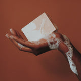 A bar soap lathered on human hand on the copper colour background. 