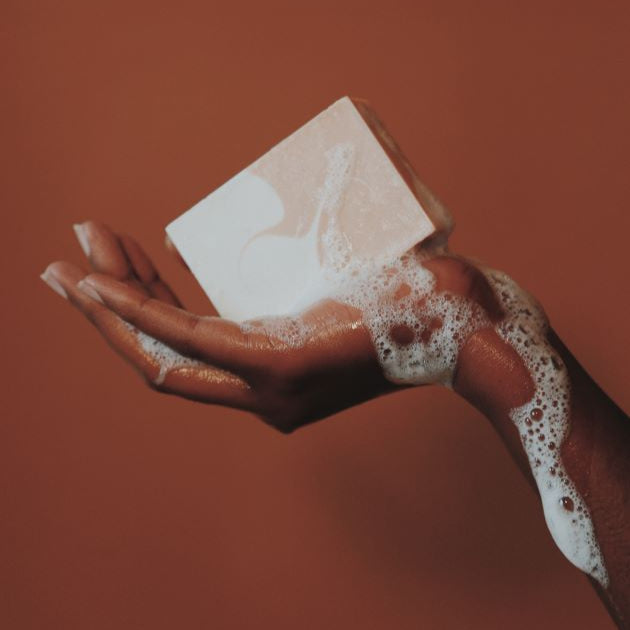 A bar soap lathered on human hand on the copper colour background. 