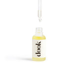 Small bottle of conditioning oil with white sticker and black dook logo. Bottle is open and the bottom of pipette hung above dropping an oil inside. On white background.