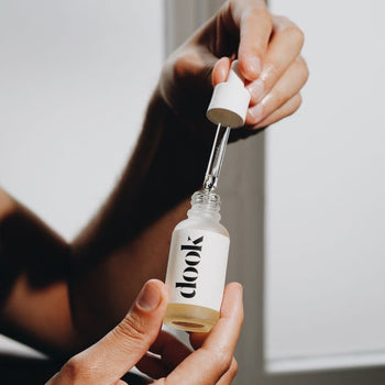 Hands holding small glass bottle of conditioning oil in one hand and a pipette in the other hand, right above the bottle. Black dook logo on the white label stick to the bottle.