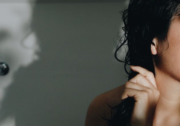 A woman in the bathroom holding her damp long black hair applying conditioning oil.
