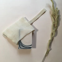 Cotton bag open with a dook soap partially hidden inside laying flat next to dried flower branch.