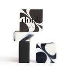 A composition of square-shaped, black and white soaps with irregular pattern with a boxed soap with a logo and copying pattern of the bar soap. Entire construction stack on the white background. 