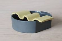 Porcelain soap dish in two pieces put together - dark grey base and citron yellow wavy top.