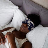 A person in bed wearing a navy print patterned merino-linen eye mask.