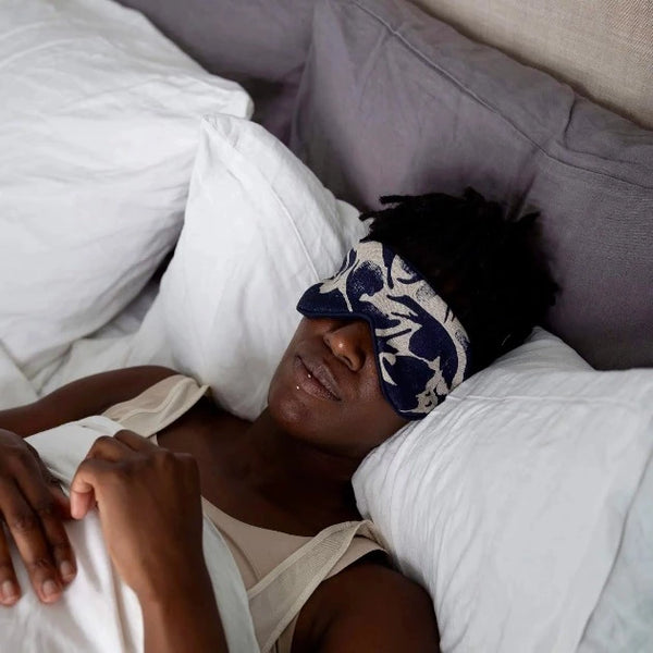A person in bed wearing a navy print patterned merino-linen eye mask.