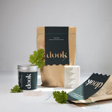 Composition of bath salts packaged in brown bags and one aluminium tin with green labels decorated with scent paired handmade soap and green leafs. All on the white background.