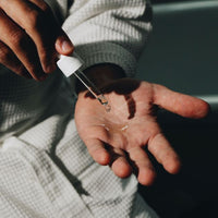 Hands using pipette with oil by person being dressed in dressing gown.
