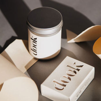 Dook's bath salts in tin and a bar of soap arranged with bits of folded white paper creating an artistic composition.