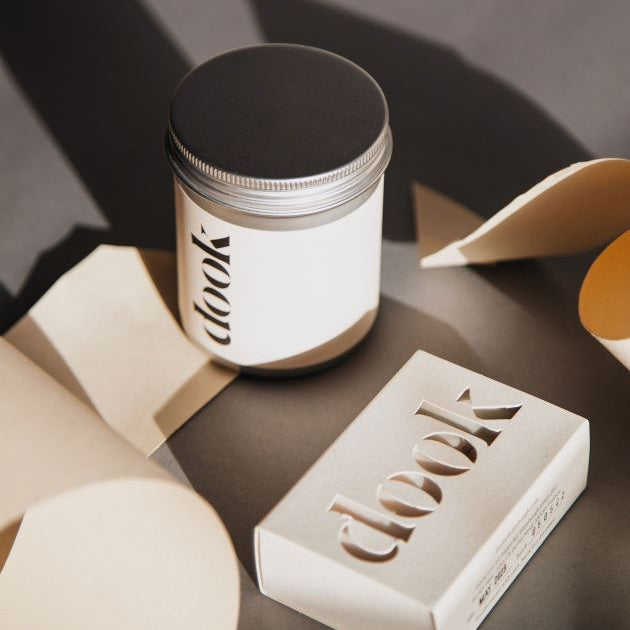 Dook's bath salts in tin and a bar of soap arranged with bits of folded white paper creating an artistic composition.