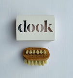 A small, wash bag size wooden nail brush with dook soap in a box lying on the white surface.