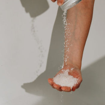A person emptying an aluminium tin of bath salts directly on a hand palm on the white bath tub background.