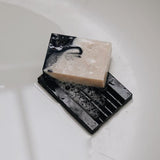 Wet 'Pure Barry' soap dish with patchouli handmade soap covered in lather placed at the bottom of the bath tub.