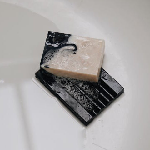 Wet 'Pure Barry' soap dish with patchouli handmade soap covered in lather placed at the bottom of the bath tub.