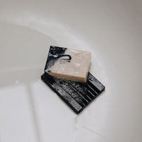 Wet 'Pure Barry' soap dish with patchouli handmade soap covered in lather placed at the bottom of the bath tub.