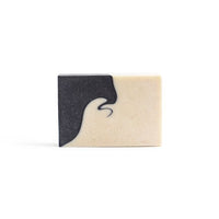 A creamy-white handmade soap with black swirly pattern on the left side on the white background.