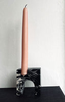 A single pink tall candle in a stone marbled black and white candle holder.