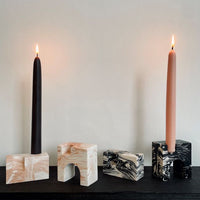 Four candle holders on a shelf, two of them with lit candles.