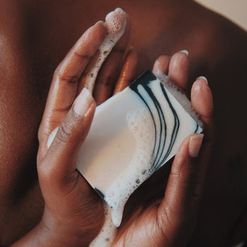 Hands holding rosemary and frankincense wet bar of soap in the background of the rest of the body.