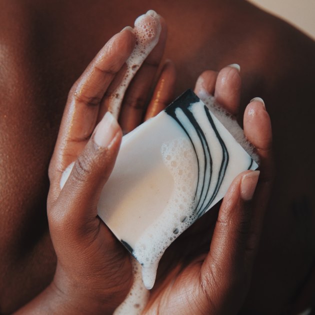Hands holding rosemary and frankincense wet bar of soap in the background of the rest of the body.