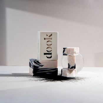 Dook soaps in two piles - as whole and crushed exposing handmade patterns. Sprinkle of a charcoal in the front, white surface and background.
