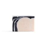 A bar of handmade soap with black and white, irregular stripe pattern in the left top corner and pink creamy colour making three quarters of the rest of the soap.