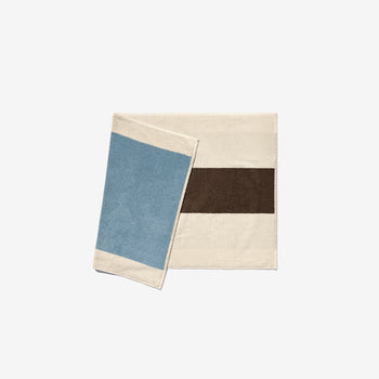 A sky blue and coffee colored bath mat with a hanging loop, designed by Karel Martens.