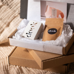An open gift box containing a scented handmade soap bar, a small sample packet, and a handwritten note, all presented on a soft surface.