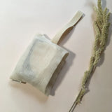 Bar of soap entirely hid in the cotton bag, laying flat next to dried flower branch.