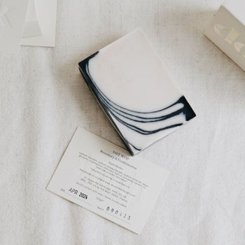 A composition of a black and white corner patterned bar soap with ingredients card as a box-free option.