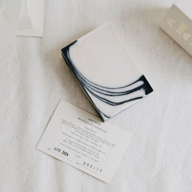 A composition of a black and white corner patterned bar soap with ingredients card as a box-free option.