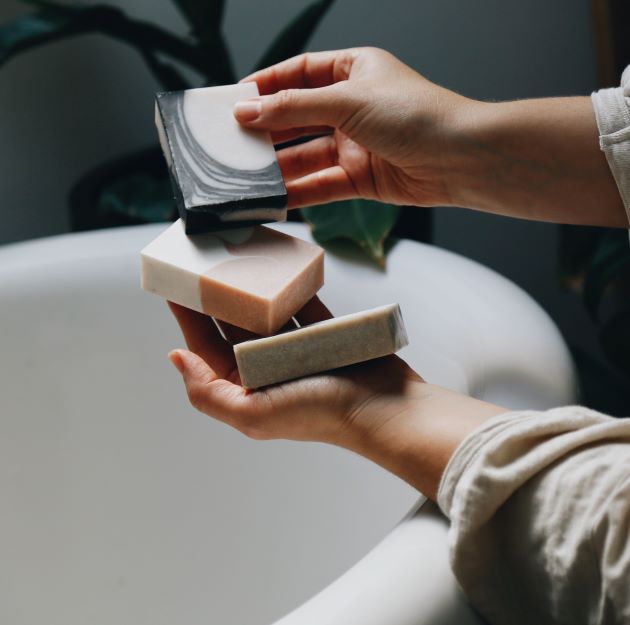 A person in the bathroom holding three bestselling handmade dook soaps in both hands and showing the unique patterns. 