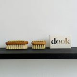 Two size oak nail brushes next to a dook soap in a box on the black shelf.
