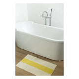 Bath mat with yellow stripe in front of a white bathtub