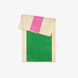 A folded bath towel with green and pink solid color blocks and a beige striped section in the corner, with a loop for hanging.