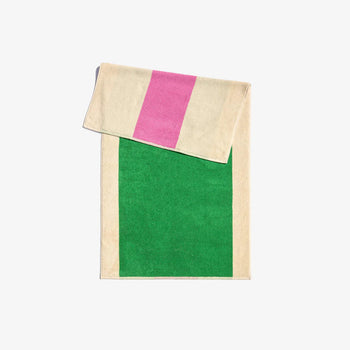 A folded bath towel with green and pink solid color blocks and a beige striped section in the corner, with a loop for hanging.